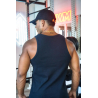 Homme vu de dos portant un débardeur noir ESSENTIAL dans une salle de musculation, casquette noire et collier doré, portant une
