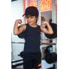 Jeune fille brunette en débardeur noir et casquette noire, flexion des bras montrant ses muscles dans une salle de sport avec un