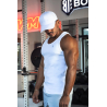 Homme musclé portant un débardeur blanc ESSENTIAL et une casquette blanche dans une salle de sport, en train de s’entraîner.