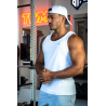 Homme musclé portant débardeur blanc ESSENTIAL, casquette arrière, chaîne dorée, en salle de sport avec poids et équipements au