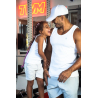 Homme musclé en débardeur blanc et casquette blanche riant avec une jeune fille au sourire éclatant, dans une salle de sport, li