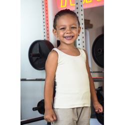 Petite garçon souriant en débardeur beige dans une salle de sport, avec des poids en arrière-plan.