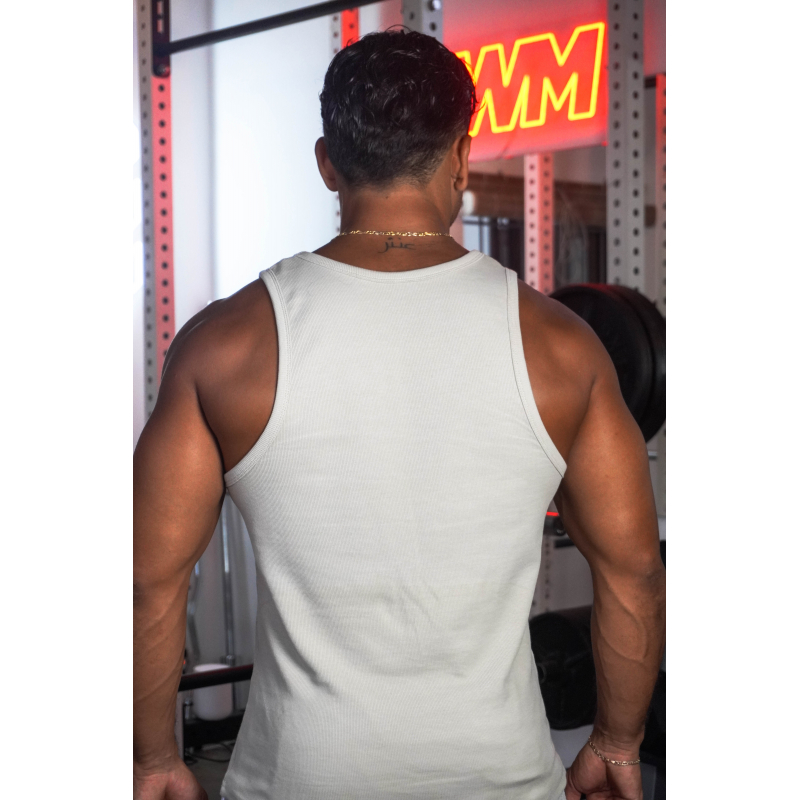 Homme vu de dos portant un débardeur beige, musculature saillante, chaîne dorée au cou, en salle de sport avec éclairage rouge.
