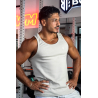 Homme musclé en débardeur ESSENTIAL beige, pose les mains sur les hanches dans une salle de sport, collier doré.