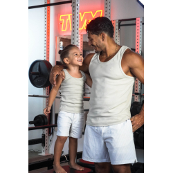Homme musclé en débardeur beige avec un jeune garçon en débardeur et shorts blancs, souriant dans une salle de sport.