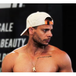 Casquette blanche en coton avec attache orange portée à l’envers sur un homme torse nu, collier doré et tatouage sur la clavicul