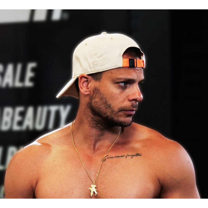 Casquette blanche en coton avec attache orange portée à l’envers sur un homme torse nu, collier doré et tatouage sur la clavicul