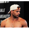 Casquette blanche en coton avec attache orange portée à l’envers sur un homme torse nu, collier doré et tatouage sur la clavicul