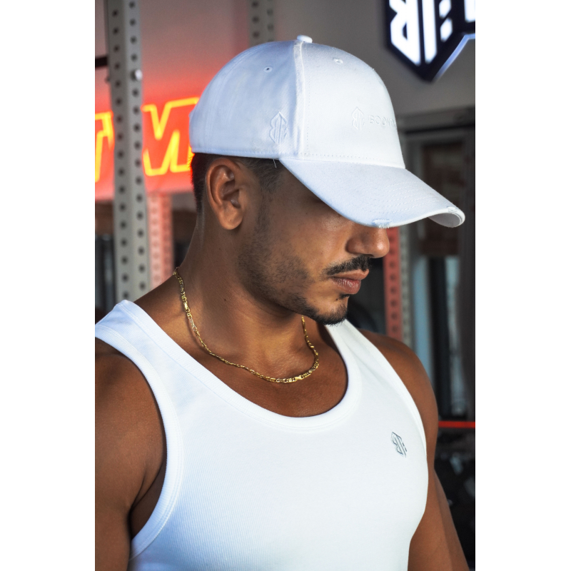 Casquette blanche en coton avec broderie légère et logo, portée par un homme musclé portant débardeur blanc et chaîne dorée.