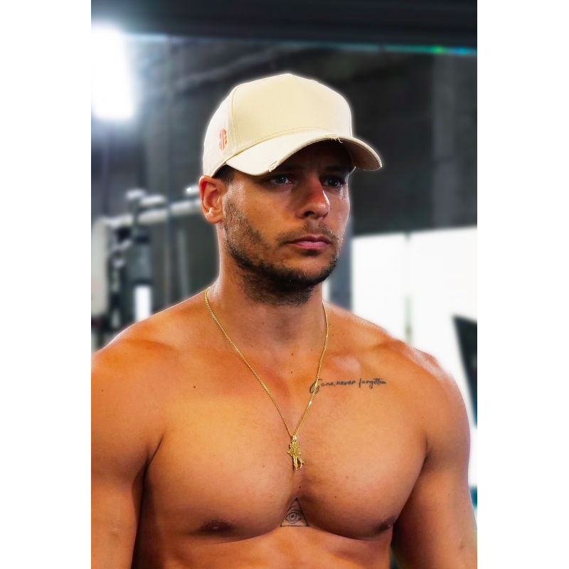 Casquette beige en coton avec attache orange portée par un homme torse nu, collier doré et tatouages visibles.
