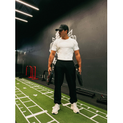 Homme musclé en t-shirt blanc et pantalon noir, portant des poids lourds dans une salle de sport moderne.