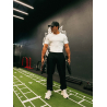 Homme musclé en t-shirt blanc et pantalon noir, portant des poids lourds dans une salle de sport moderne.
