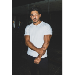 Homme musclé en t-shirt blanc ESSENTIAL, pose les bras croisés dans un décor sombre.