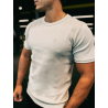T-shirt ESSENTIAL beige ajusté sur un homme, logo discret sur la poitrine, fond sombre.