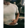 Homme portant T‑shirt ESSENTIAL beige près du torse, logo discret sur la poitrine, scène en arrière-plan floue.