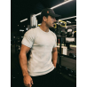 Homme portant t‑shirt ESSENTIAL beige dans une salle de sport, casquette noire et tricot serré, en posture décontractée.