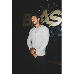 Homme musclé en t-shirt blanc à manches longues, fond noir avec logo beige et éclats décoratifs, pose décontractée.
