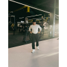 Homme portant un t-shirt blanc et pantalon noir dans une salle de sport, pieds en sneakers blancs, casquette noire, avec poids e