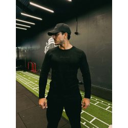Homme portant t-shirt noir à manches longues ESSENTIAL, casquette noire, dans une salle de sport au sol vert avec lignes blanche