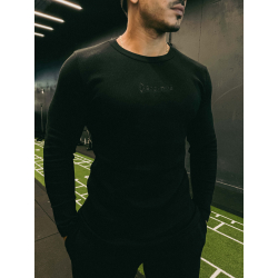 Homme portant un t-shirt noir à manches longues ESSENTIAL noir, debout en salle de sport, avec chaînes dorées et fond sombre.