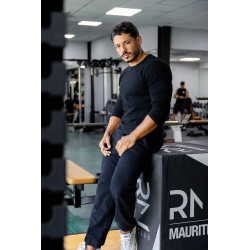 Homme musclé en vêtements noirs, debout près d’un banc et d’un box de plyométrie dans une salle de sport moderne.