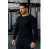 Homme musclé dans une salle de sport, chemise noire à manches longues ESSENTIAL noir, regard posé, chaîne dorée, ambiance gym.