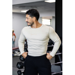 Homme musclé en t-shirt manches longues beige, pose les mains sur les hanches dans une salle de sport.