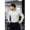 Homme musclé en t-shirt manches longues beige, pose les mains sur les hanches dans une salle de sport.