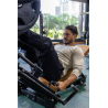 Homme musclé en T-shirt beige à manches longues, assis sur une machine de musculation, engageant les jambes sur une presse, gym