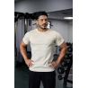 Homme musclé dans une salle de sport portant un t-shirt esssential beige clair, main sur les hanches, arrière-plan de matériel d