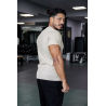 Homme musculé en t-shirt beige ESSENTIAL, vue de profil dans une salle de sport, portant pantalon noir.