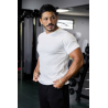 Homme musclé portant un t-shirt blanc ESSENTIAL, près d’un équipement de gym, look soigné et bandeau sur la poitrine.