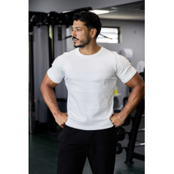 Homme musclé en t-shirt ESSENTIAL blanc, debout en salle de sport, poings sur les hanches, regard sur le côté.