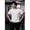 Homme musclé en t-shirt ESSENTIAL blanc, debout en salle de sport, poings sur les hanches, regard sur le côté.
