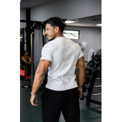 Homme musclé vu de dos dans une salle de sport, porte T-shirt blanc ESSENTIAL, cheveux courts, pantalon noir, en train de se dét