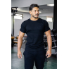 Homme musclé portant t-shirt noir ESSENTIAL noir, en salle de sport, regard vers la droite, cheveux foncés et barbe légère.