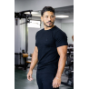 Homme musclé en t-shirt noir ESSENTIAL, debout dans une salle de sport, muscles visibles et expression concentrée.